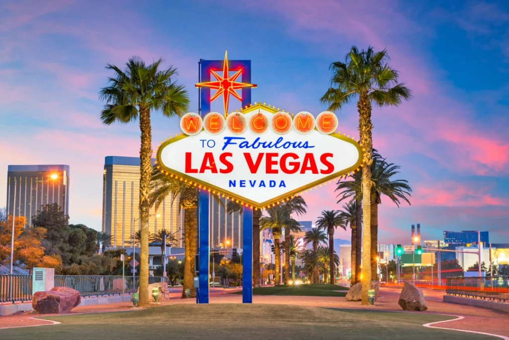 Het verlichte welkomstbord van Las Vegas met palmbomen en de skyline op de achtergrond bij zonsondergang