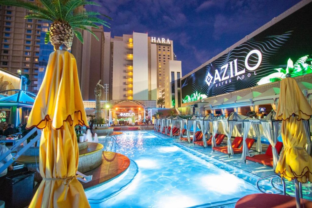 Een verlicht zwembad met loungebedden en gele parasols ligt voor het hotel Sahara in de avond in Las Vegas