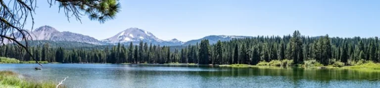 Panoramisch uitzicht over een meer met dennenbos aan de oever en de vulkaantop van Lassen Peak op de achtergrond