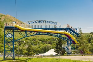 Lange gele waterglijbaan op een blauw frame met het opschrift Lava Hot Springs, tegen een groene heuvel
