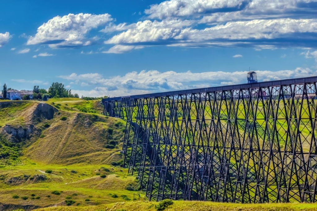 Lange zwarte stalen spoorbrug op hoge pijlers overspant een groene vallei onder een wolkenlucht