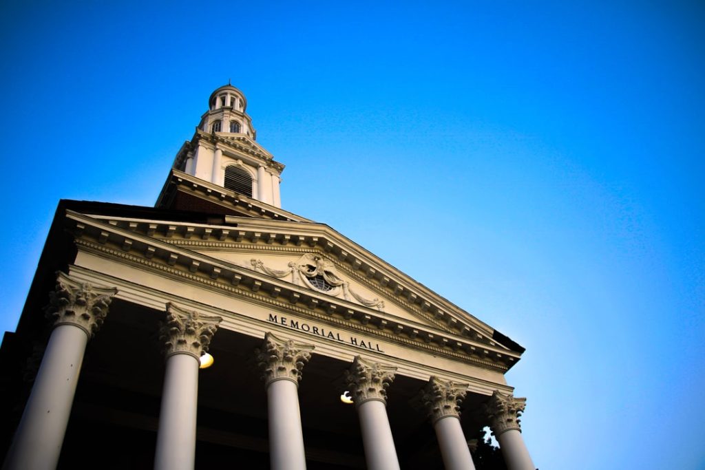 Blik omhoog naar de gevel van Memorial Hall met een rij witte zuilen en een torentje tegen een strakblauwe lucht