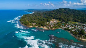 Luchtfoto van een klein dorp met kleurrijke daken tussen dicht regenwoud aan een baai met turkoois water in Limón