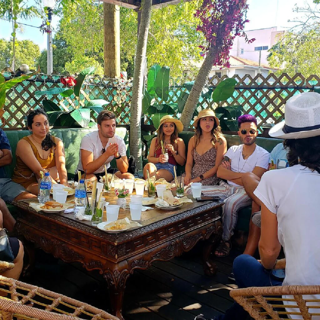 Een groep reizigers zit gezellig aan een tafel vol drankjes en gerechten op een groen terras in Little Havana
