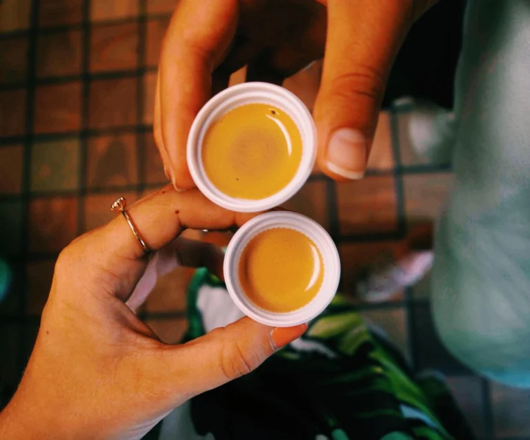 Twee handen houden kleine witte bekertjes met sterke gele Cubaanse koffie omhoog tijdens een rondleiding in Little Havana