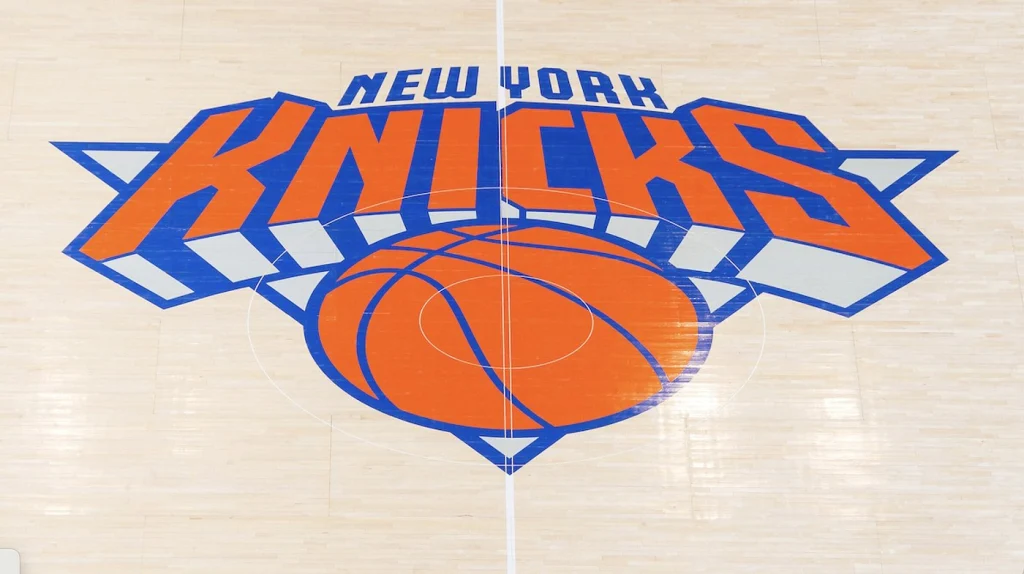 Groot oranje en blauw logo van de New York Knicks midden op de houten vloer van een basketbalveld