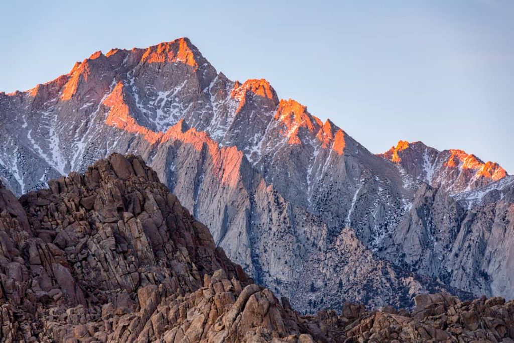 Rotsachtige bergtop kleurt oranje door alpengloed bij zonsopkomst, gezien vanaf een rotsachtige voorgrond