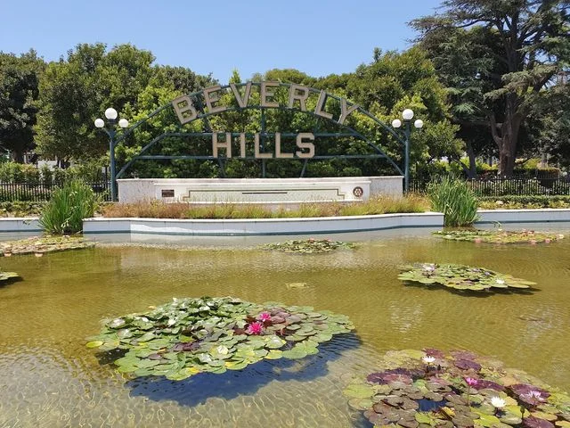 Metalen bord met de tekst Beverly Hills staat bij een vijver vol waterlelies omringd door bomen