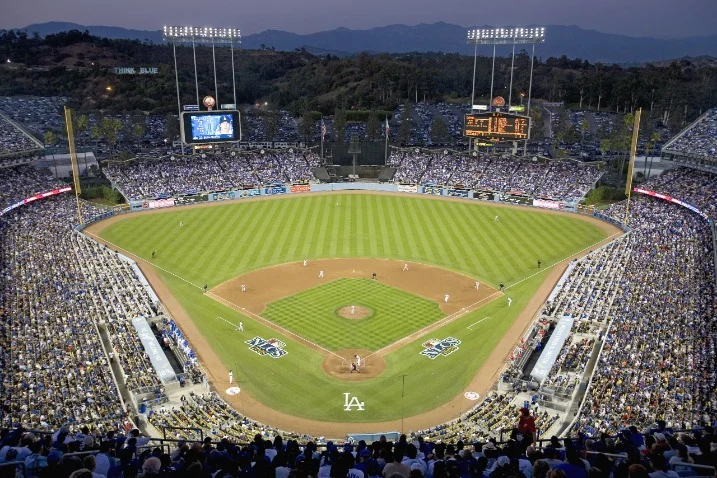 Volle tribunes rondom een verlicht speelveld tijdens een avondwedstrijd in Dodger Stadium met heuvels op de achtergrond