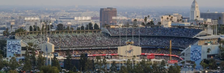 Panoramisch uitzicht over een volledig gevuld honkbalstadion met het speelveld en de skyline van Los Angeles op de achtergrond