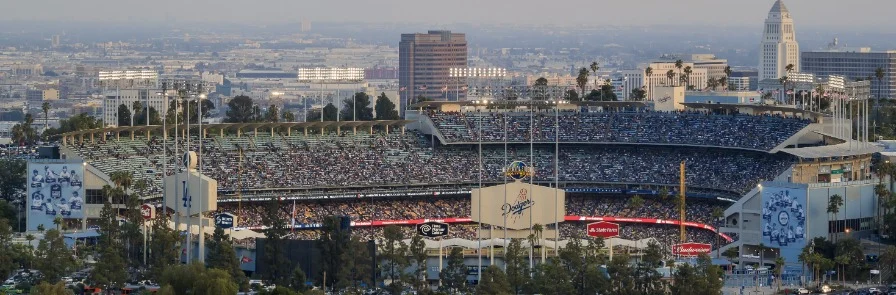 Panoramisch uitzicht over een volledig gevuld honkbalstadion met het speelveld en de skyline van Los Angeles op de achtergrond