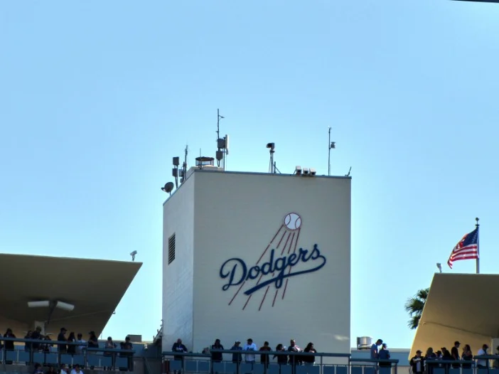 Groot Dodgers logo met een honkbal en vlaggen op de gevel van een gebouw bij het stadion met toeschouwers ervoor