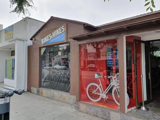 Gevel van een fietsverhuurwinkel met een witte fiets uitgestald in een rood verlichte etalage in Los Angeles
