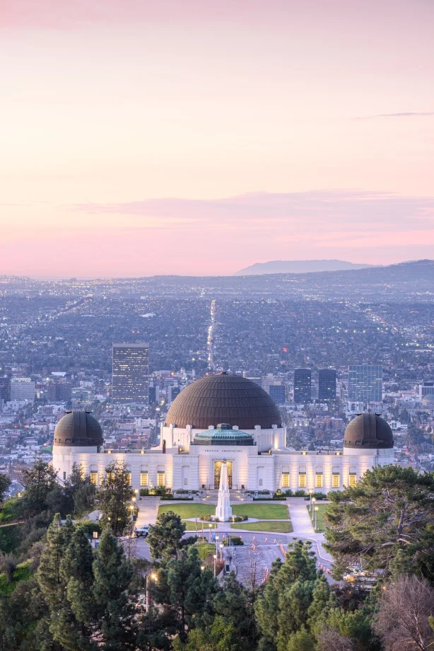 Luchtfoto van het Griffith Observatory met zijn koepels boven de wolkenkrabbers van Los Angeles tijdens een roze zonsondergang