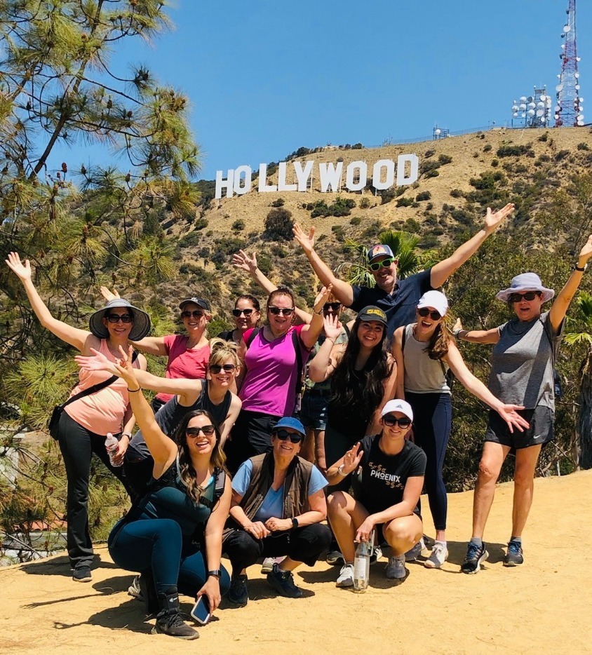 Een uitgelaten groep reizigers steekt de armen omhoog voor het Hollywood-bord op de heuvel in Los Angeles