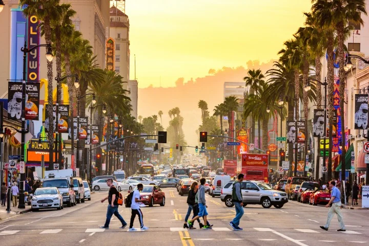 Voetgangers steken de drukke Hollywood Boulevard over tussen neonreclames en verkeer bij zonsondergang