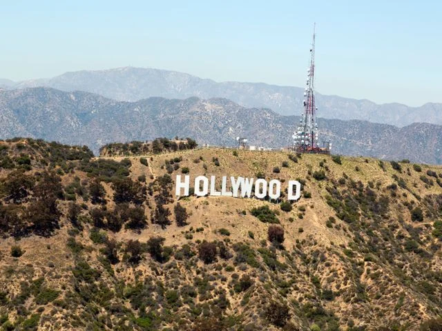 De witte letters van het Hollywood Sign op een droge heuvel met bergen op de achtergrond en een zendmast ernaast