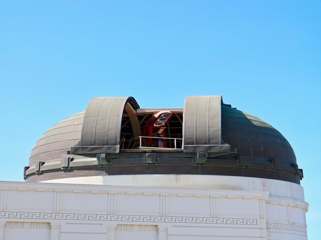 Open metalen koepel met een grote telescoop op het dak van het Griffith Observatory tegen een strakblauwe hemel