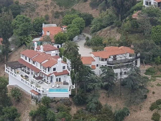 Luchtfoto van een grote witte villa met rode dakpannen, een zwembad en veel groen op een heuvel bij Los Angeles
