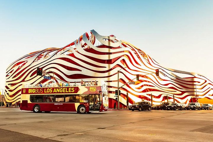 Rode sightseeingbus rijdt voorbij het opvallende rood met gouden gevel van het Petersen Automotive Museum in Los Angeles