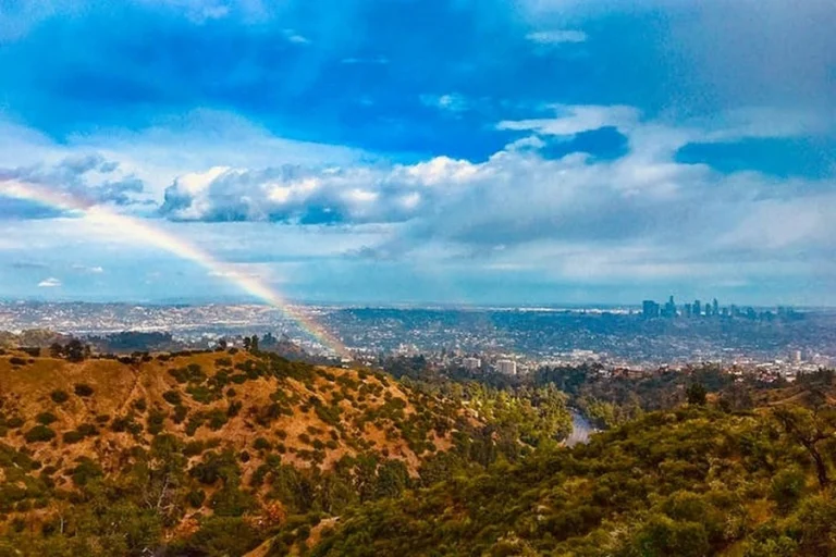 Uitzicht vanaf een groene heuvel bij Los Angeles op de skyline in de verte met een regenboog aan de blauwe wolkenlucht