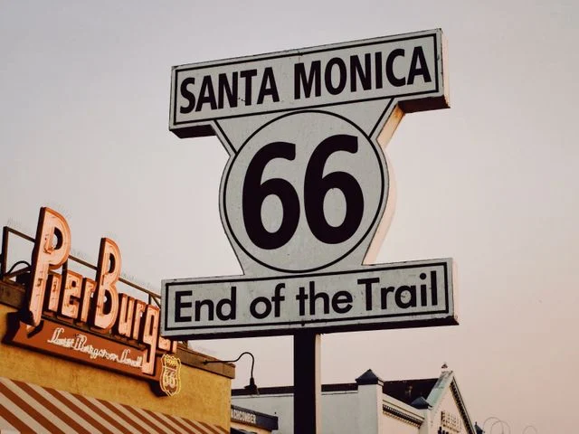 Historisch bord met de tekst Santa Monica 66 End of the Trail naast een neonreclame van een hamburgertent