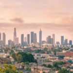 Wolkenkrabbers van het centrum van Los Angeles steken af tegen een roze avondlucht met palmbomen en woonwijken op de voorgrond