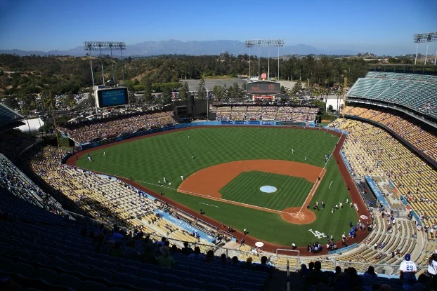 Uitzicht vanaf de tribune over het groene speelveld van Dodger Stadium met spelers en gevulde tribunes onder een blauwe lucht