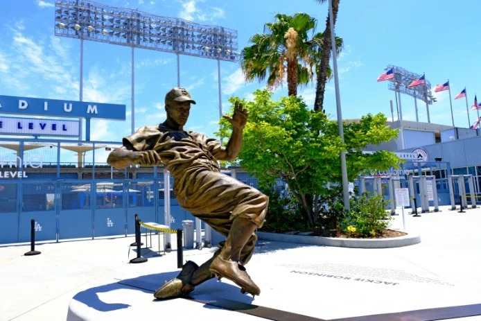 Bronzen standbeeld van een glijdende honkballer met palmbomen en vlaggen op de achtergrond bij Dodger Stadium