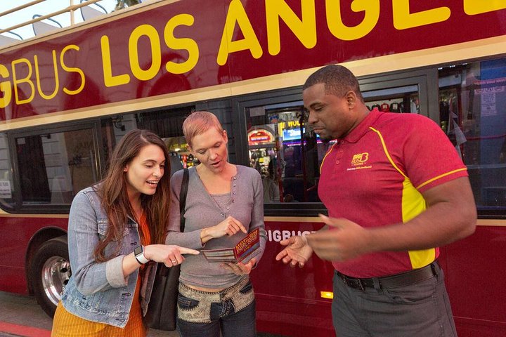 Twee vrouwen bekijken samen een tourbrochure terwijl een medewerker van de sightseeingbus in Los Angeles uitleg geeft