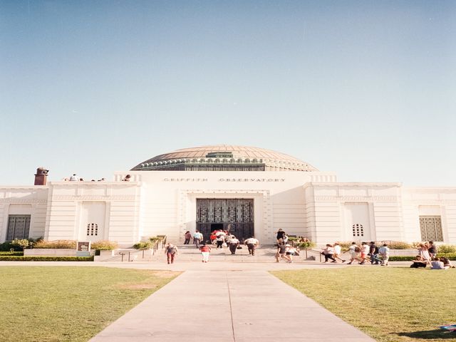 Bezoekers lopen over het grasveld en de trappen voor de witte koepelgevel van het Griffith Observatory
