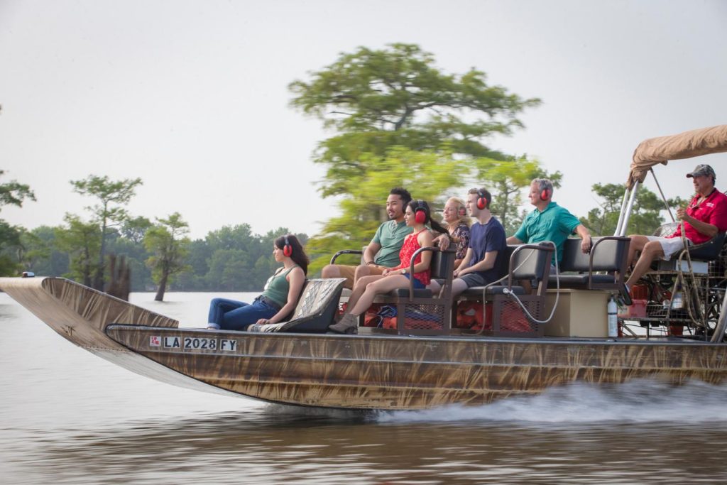 Groep toeristen met gehoorbeschermers vaart op een airboat door een moerasgebied in Louisiana omringd door bomen
