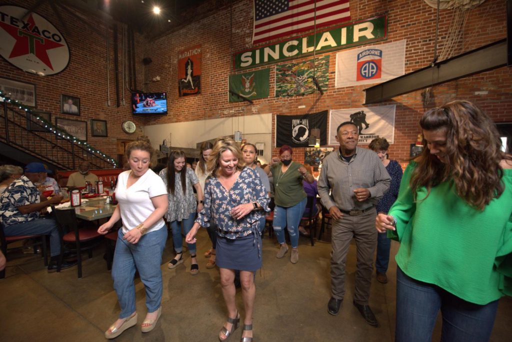 Groep bezoekers danst uitgelaten in een sfeervol Cajun restaurant met bakstenen muren en Amerikaanse vlaggen in Louisiana