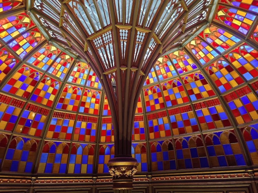 Kleurrijke gebrandschilderde glazen koepel in rood, blauw en geel boven een sierlijke zuil in een historisch overheidsgebouw