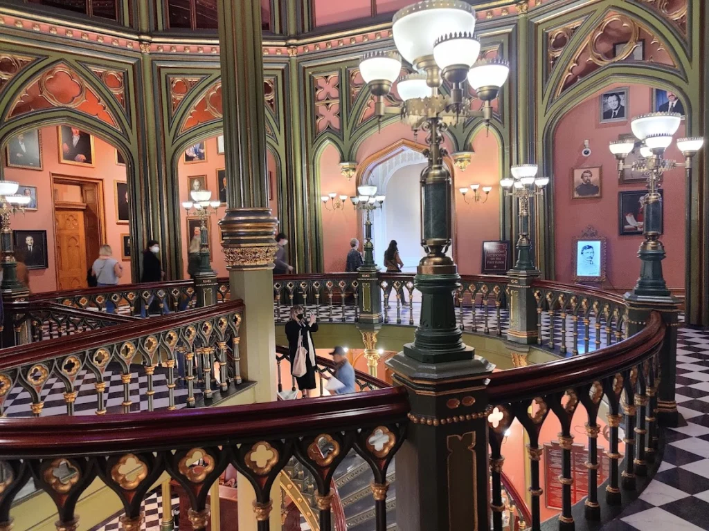 Rijk versierde gotische trappenhal met sierlijke balustrades, kroonluchters en portretten aan de muren, met bezoekers op de bordessen