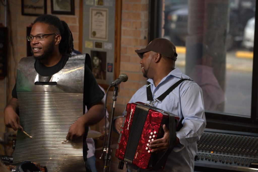 Muzikant speelt een rode accordeon terwijl een percussionist meespeelt in een sfeervol Cajun restaurant met bakstenen muren in Louisiana