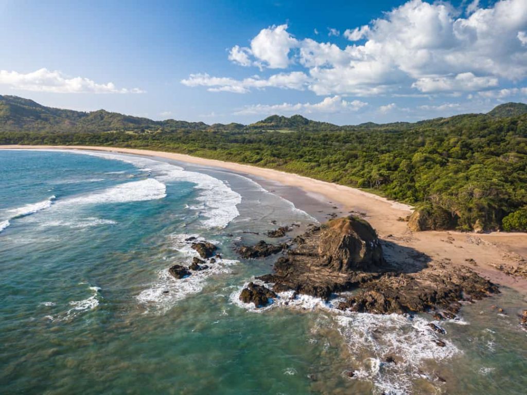 Luchtfoto van een verlaten zandstrand met rotsformatie en golven, omgeven door groen regenwoud in Costa Rica