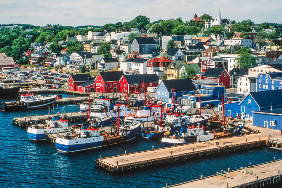 Rode en witte gebouwen en verschillende vissersboten liggen aan de kade van het historische havenstadje Lunenburg met kleurrijke huizen op de heuvel erachter