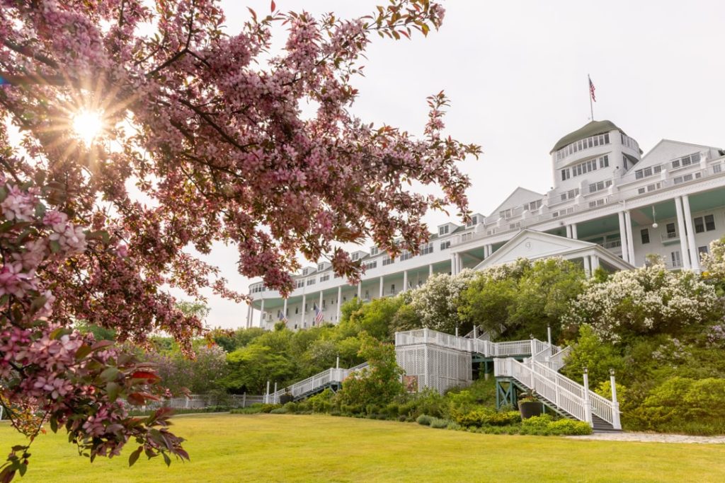 Wit Grand Hotel met lange veranda en torentje, met een roze bloeiende boom en de zon op de voorgrond