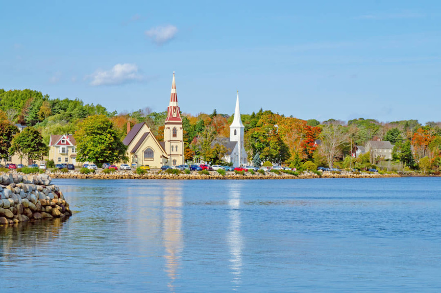 Drie karakteristieke witte kerken met spitse torens staan naast elkaar aan de waterkant van Mahone Bay en weerspiegelen in het rustige water