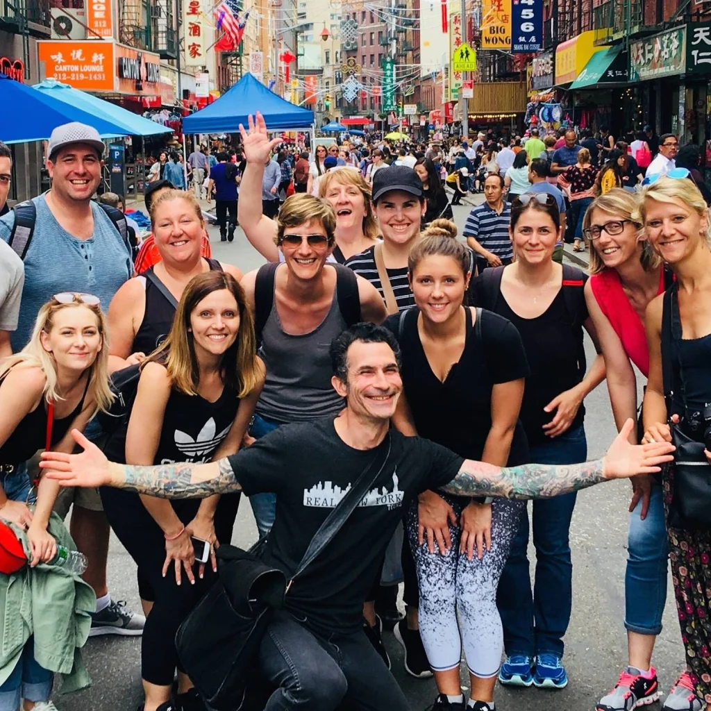 Grote groep lachende reizigers poseert op een drukke straat met Chinese uithangborden en lantaarns in Chinatown in Manhattan