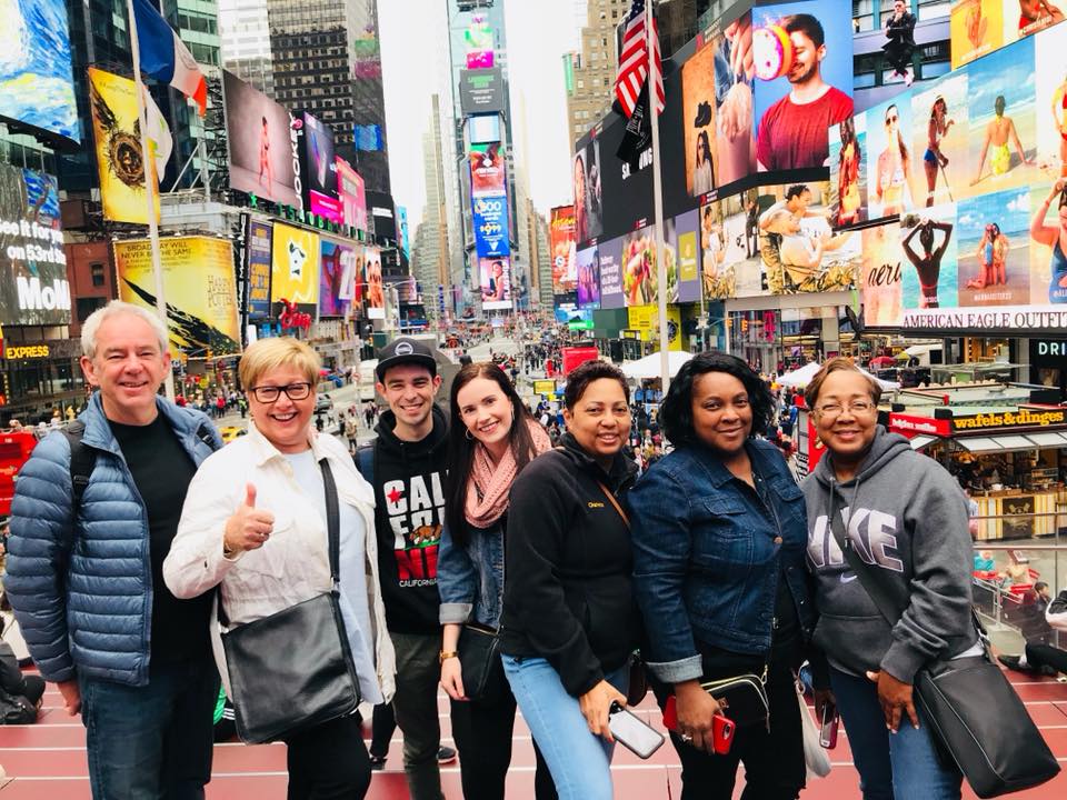 Groep reizigers poseert op Times Square met grote lichtreclames en billboards op de achtergrond in Manhattan