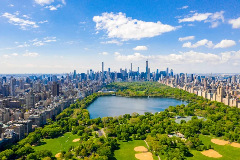 Luchtfoto van het groene Central Park met een vijver, sportvelden en de wolkenkrabbers van Manhattan aan de horizon