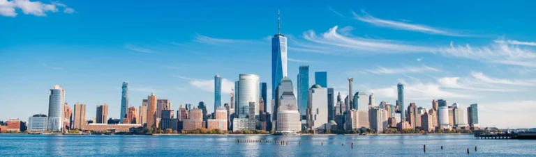 Breed panorama van de wolkenkrabbers van Lower Manhattan gezien vanaf het water onder een heldere blauwe lucht