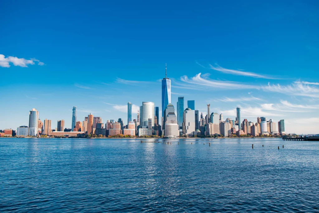 Wolkenkrabbers van Lower Manhattan gezien vanaf het water met een helderblauwe lucht en een enkele wolkensliert