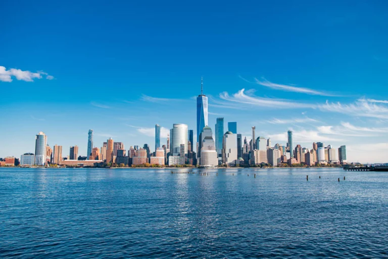 Wolkenkrabbers van Lower Manhattan gezien vanaf het water met een helderblauwe lucht en een enkele wolkensliert