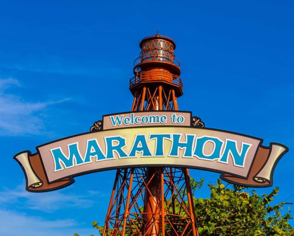 Bord met opschrift Welcome to Marathon voor een oude ijzeren uitkijktoren tegen een strakblauwe lucht