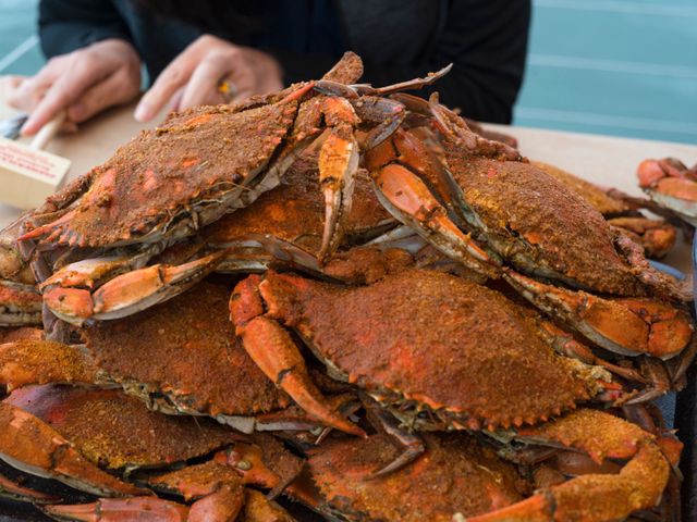 Stapel felrode gestoomde krabben bedekt met kruiden op een dienblad terwijl iemand er twee krabben uit pakt
