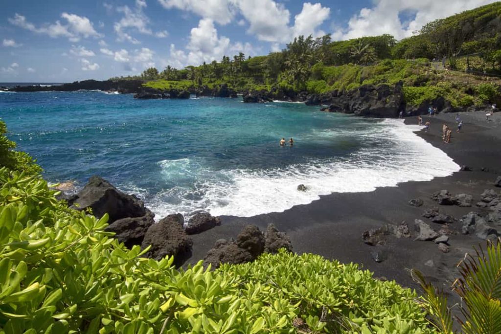 Zwemmers in een turkooizen baai omringd door zwart lavagesteente en groene begroeiing bij Waianapanapa op Maui