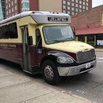 Een rood met beige toerbus van Backbeat Tours staat geparkeerd langs een straat in Memphis met winkelpanden op de achtergrond